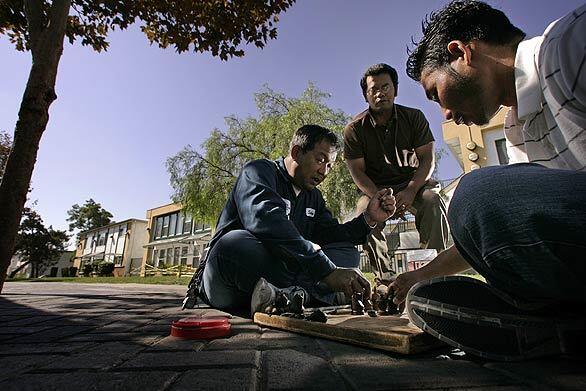 One day after Thursday's raid, Samaky Hay, 49, left, and Rith Bin, 39, play chess on the sidewalk in front of Bishop Manor. A 10-month investigation into alleged gang activity at the Santa Ana apartment complex led to the bust.