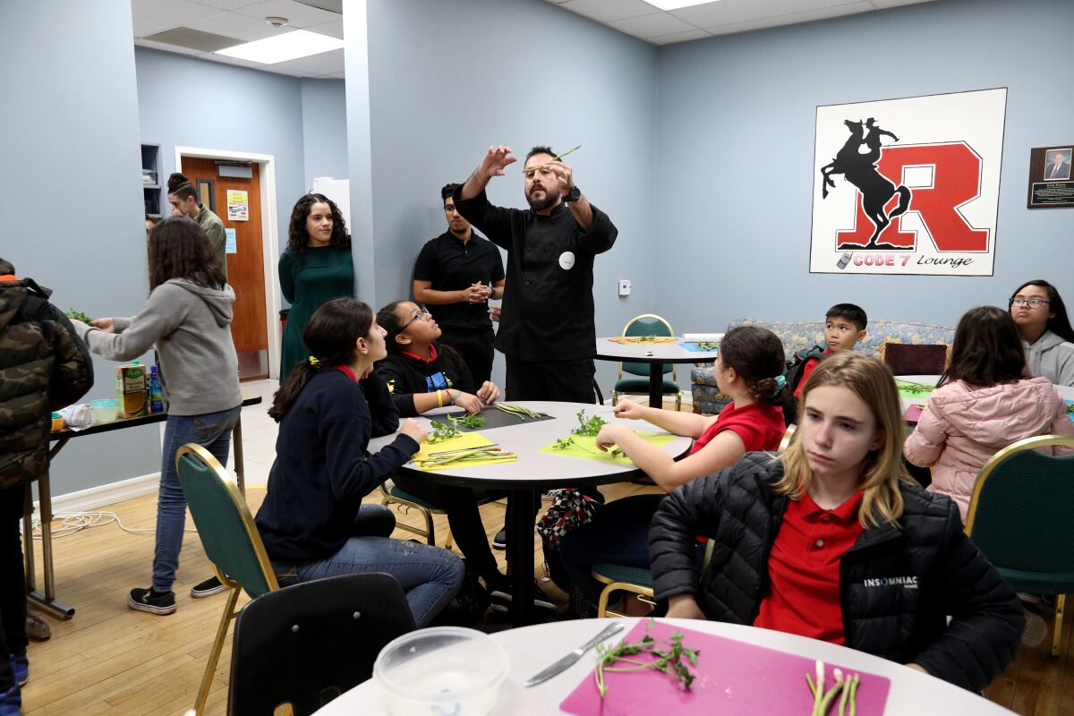 Chef Santiago Segura shows cooking students where to cut the vegetables at the Roosevelt Middle School enrichment culinary class on Thursday. The students made fettuccine Alfredo.