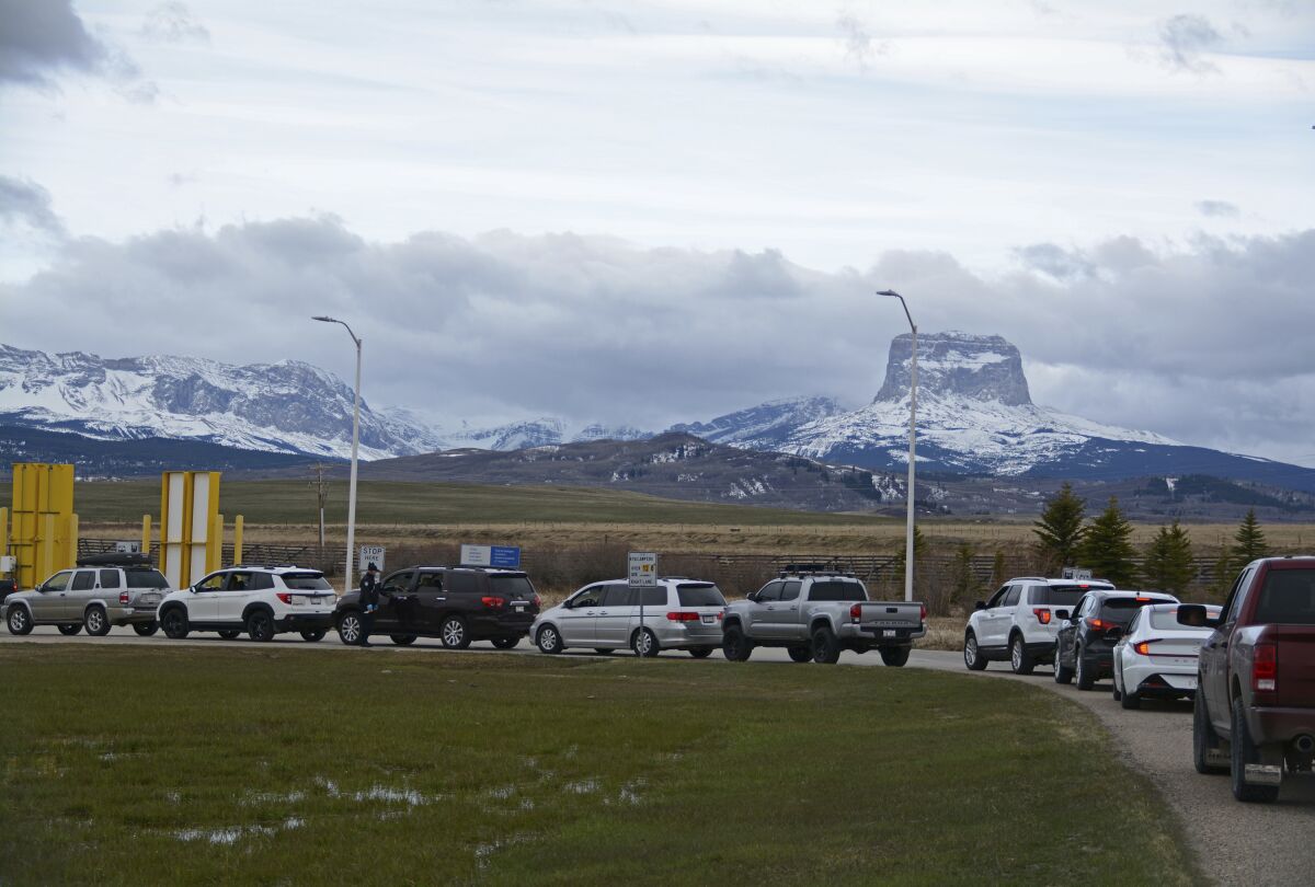 In this Thursday, April 29, 2021, photo, Canadians drive-in at the Piegan-Carway border to receive a COVID-19 from the Blackfeet tribe near Babb, Mont. The Chief Mountain, sacred to the Blackfeet tribe towers, are seen in the background. The Blackfeet tribe gave out surplus vaccines to its First Nations relatives and others from across the border. (AP Photo/Iris Samuels)