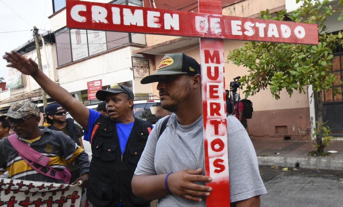 Un migrante sostiene una cruz en que se lee "Crimen de Estado. Muertos", 
