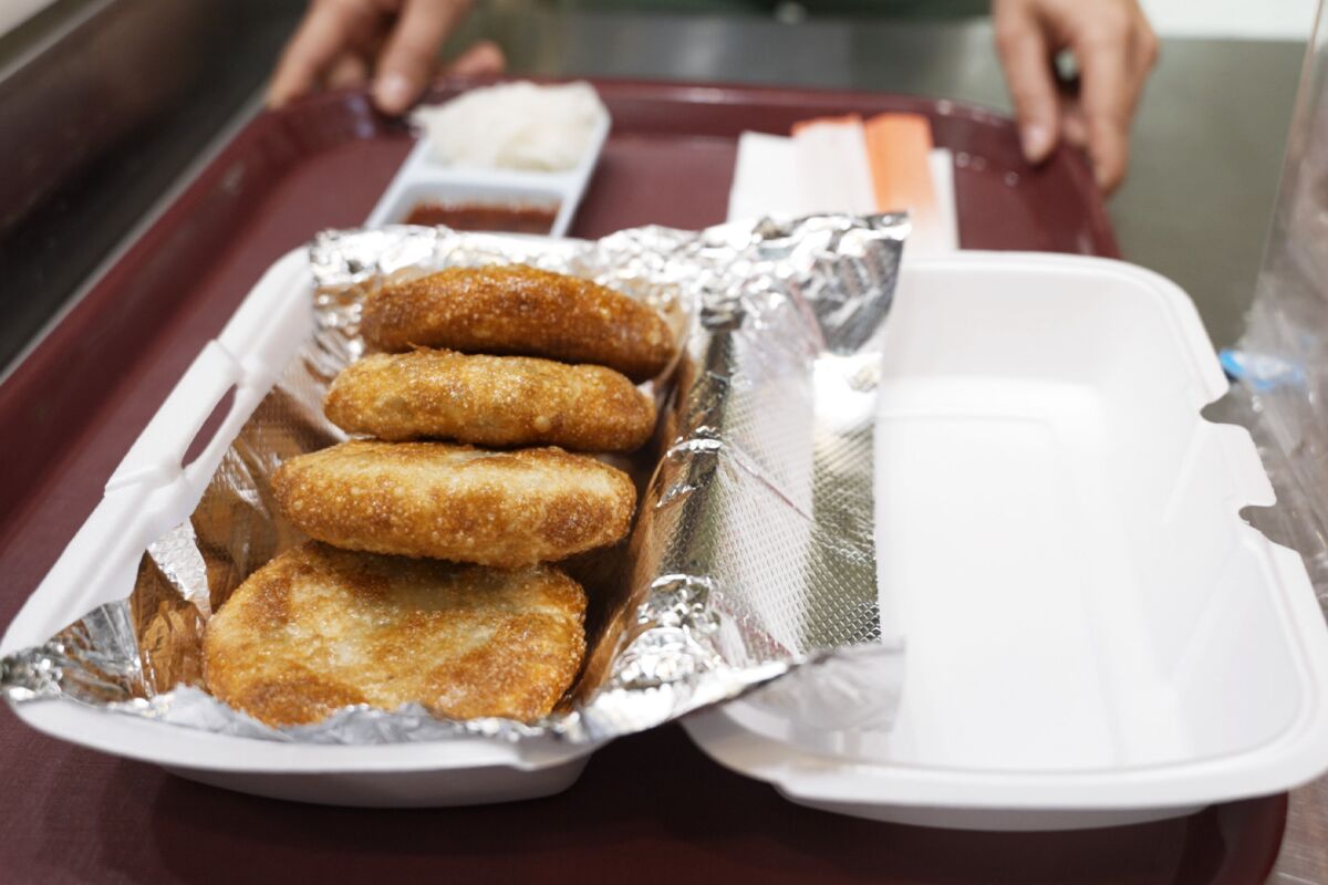 Closeup of fried dumplings on top of foil in a to-go container on a tray.