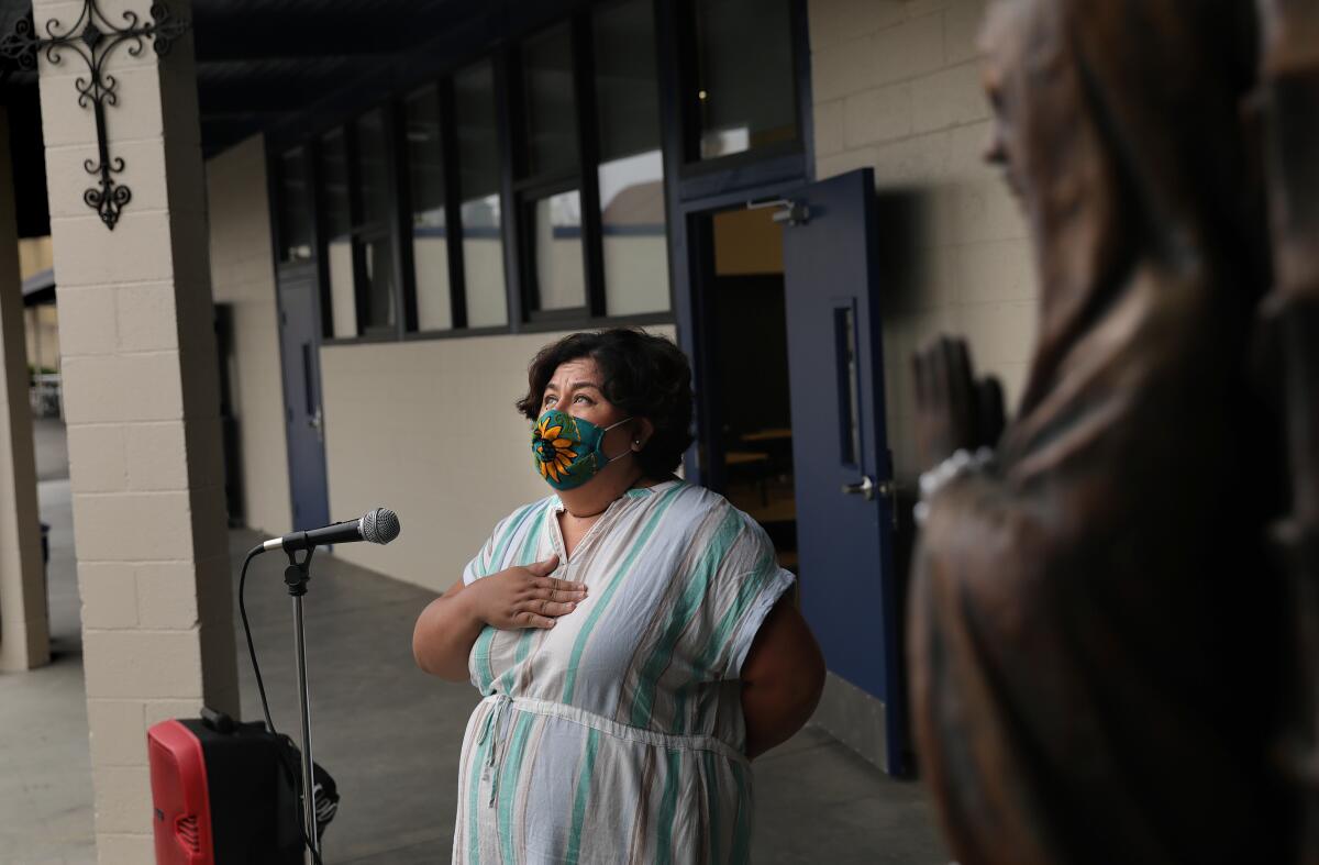 A masked woman recites the Pledge of Allegiance with her hand over her heart