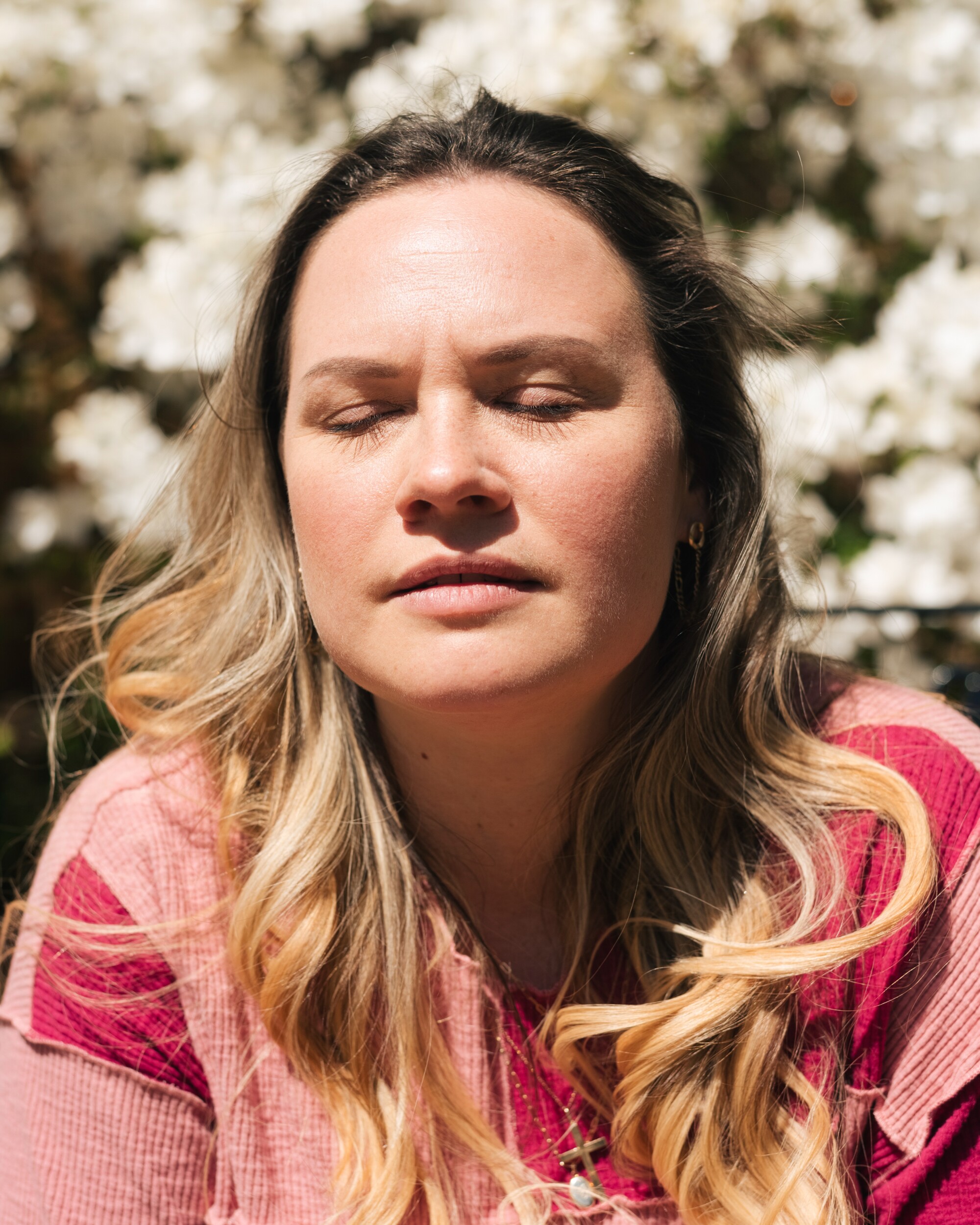 A woman closes her eyes in her backyard and leans her face up to the sun.