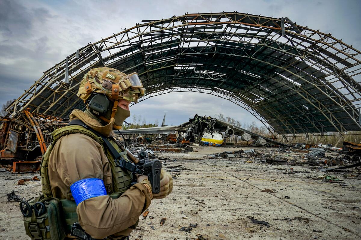 A Ukrainian soldier passes a hangar with a destroyed plane inside  