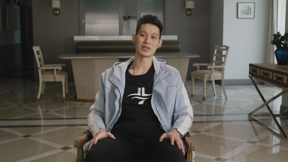 a man in a zip-up hoodie and a black t-shirt sits on a chair in the middle of a room