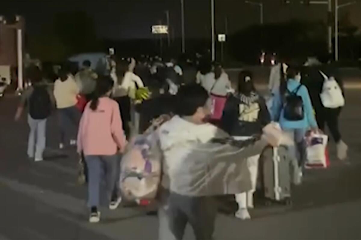 People with suitcases and bags are seen leaving a Foxconn compound in the dark.