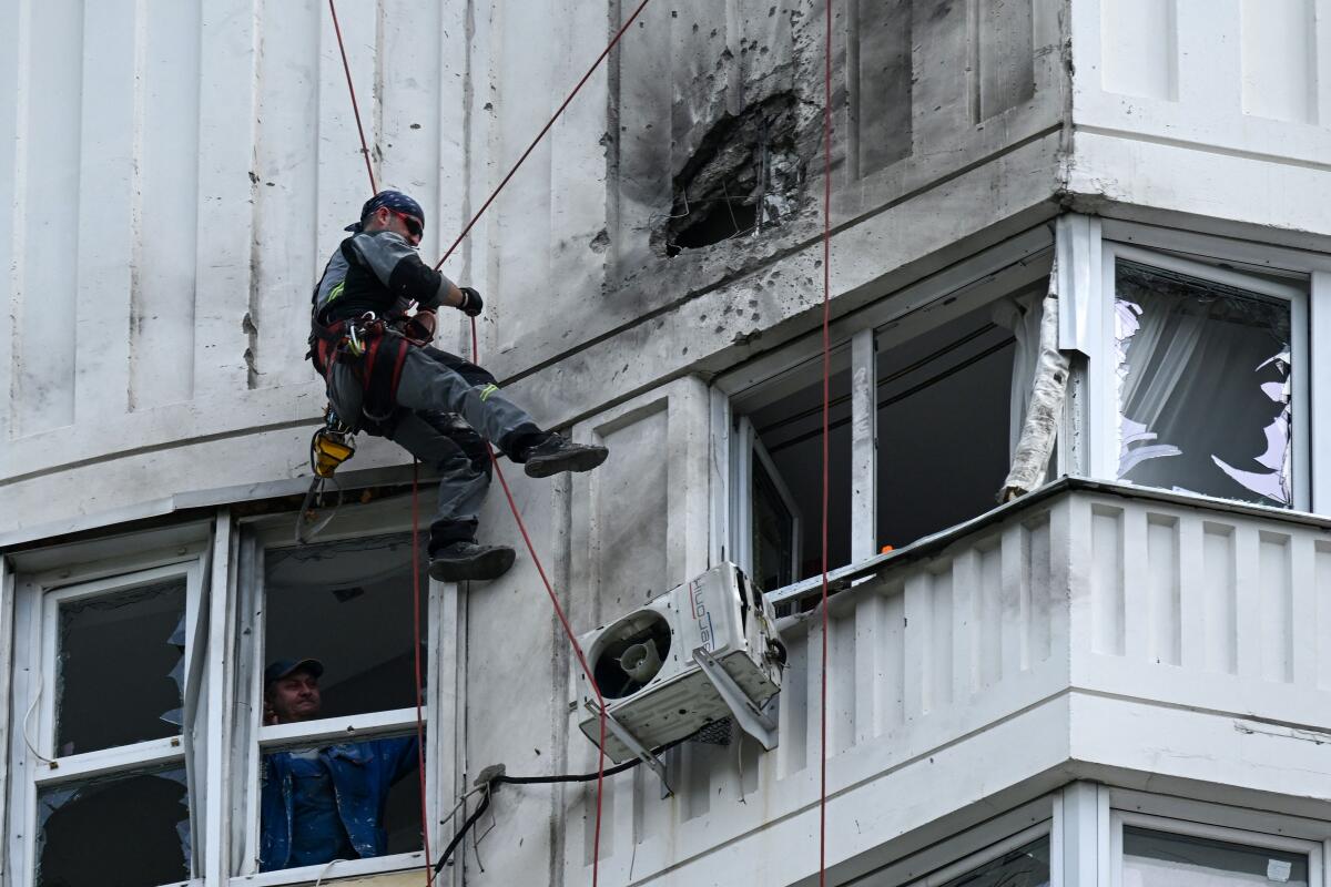 A person in a harness scaling a building with blown-out windows and a hole in the wall