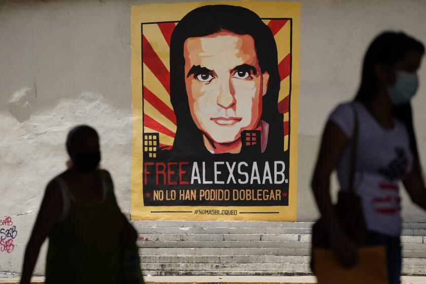 FILE - In this Thursday, Sept 9, 2021, file photo, pedestrians walk near a poster asking for the freedom of Colombian businessman and Venezuelan special envoy Alex Saab, in Caracas, Venezuela. Saab, a top fugitive close to Venezuela's socialist government has been put on a plane to the U.S. to face money laundering charges, a senior U.S. official confirmed Saturday, Oct. 16, 2021. (AP Photo/Ariana Cubillos, File)