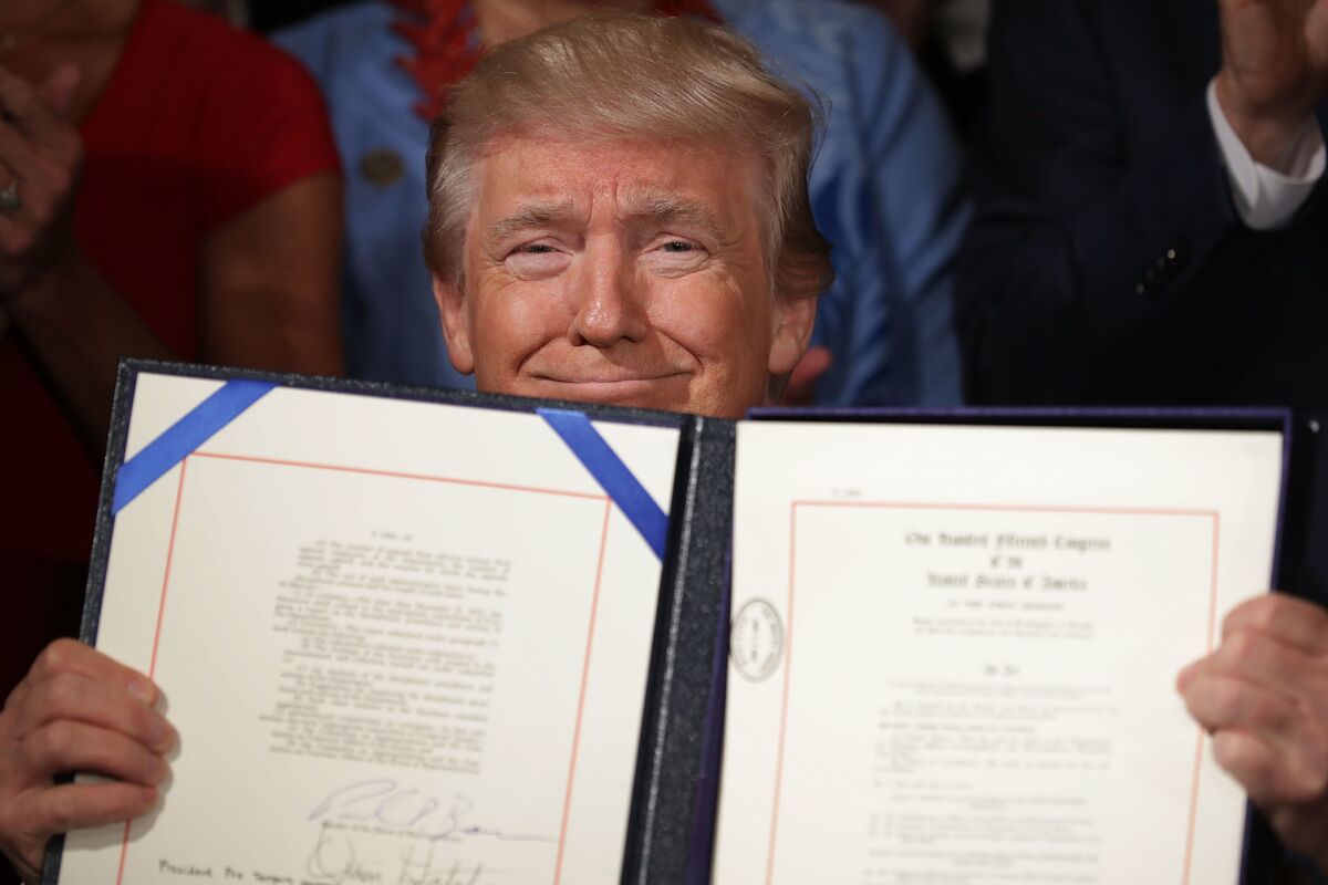 President Trump smiles while holding an open certificate holder with a just-signed bill