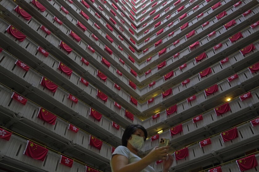 A woman walks past the Chinese and Hong Kong flags hanging from a residential building to celebrate the 25th anniversary of Hong Kong handover to China, at a public housing estate, in Hong Kong, Saturday, June 25, 2022. President Xi Jinping will participate in next week's celebrations of the 25th anniversary of the return of Hong Kong to China, the government said Saturday, but it left unclear whether he will visit the former British colony for the highly symbolic event after a crackdown on a pro-democracy movement. (AP Photo/Kin Cheung)