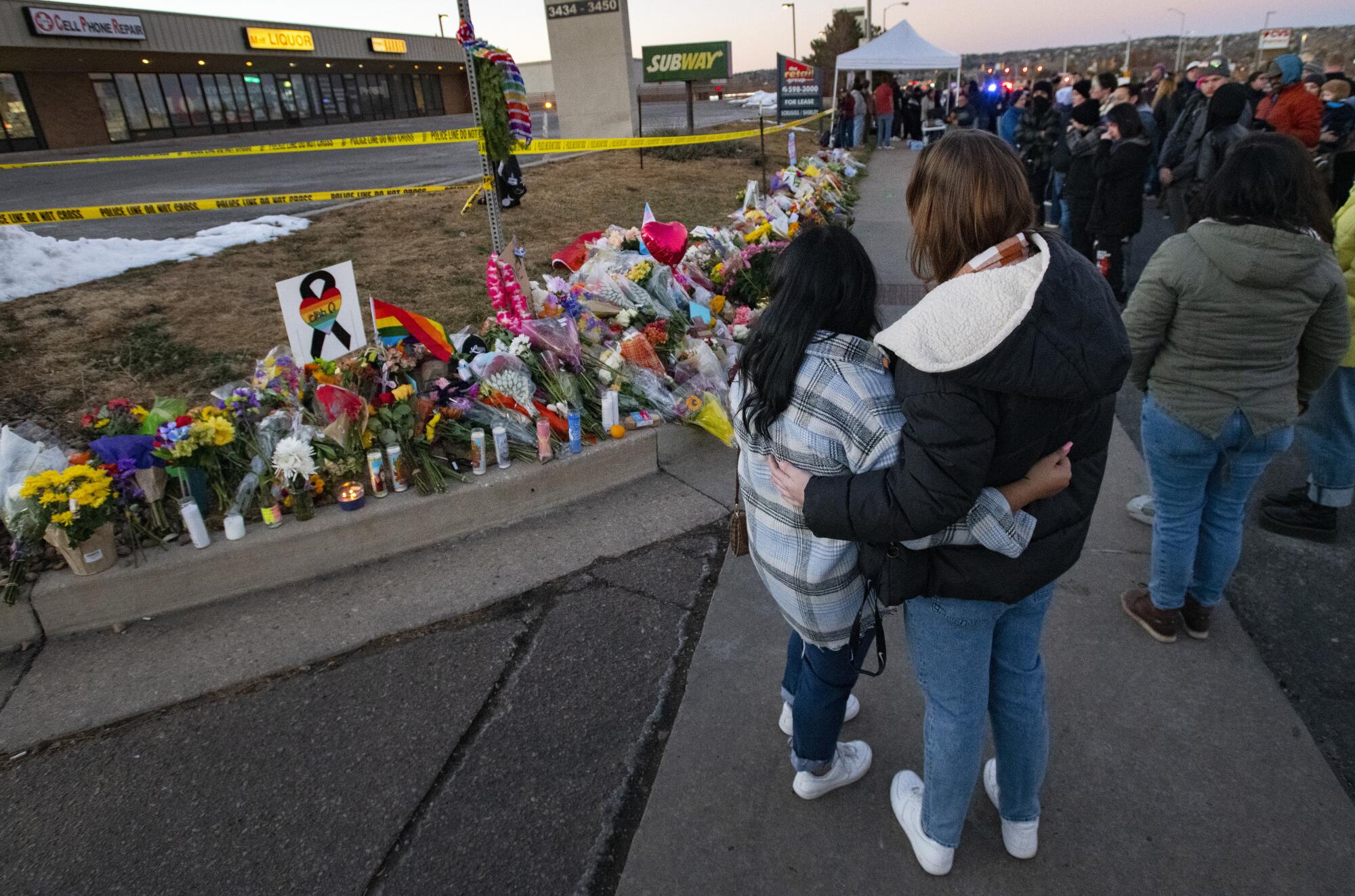 People gather around a memorial Sunday for the victims of Saturday's fatal shooting at Club Q.