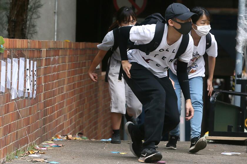 People wearing face masks duck down as they walk at Hong Kong Polytechnic University in Hong Kong, Tuesday, Nov. 19, 2019. About 100 anti-government protesters remained holed up at a Hong Kong university Tuesday as a police siege of the campus entered its third day. (AP Photo/Achmad Ibrahim)