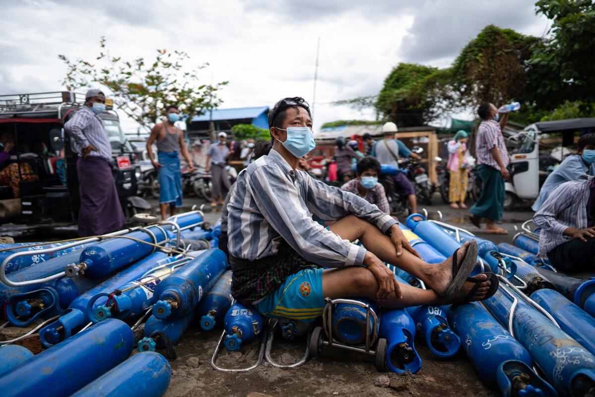 A man sits on a pile of empty oxygen canisters while waiting to refill them outside a factory in Mandalay.
