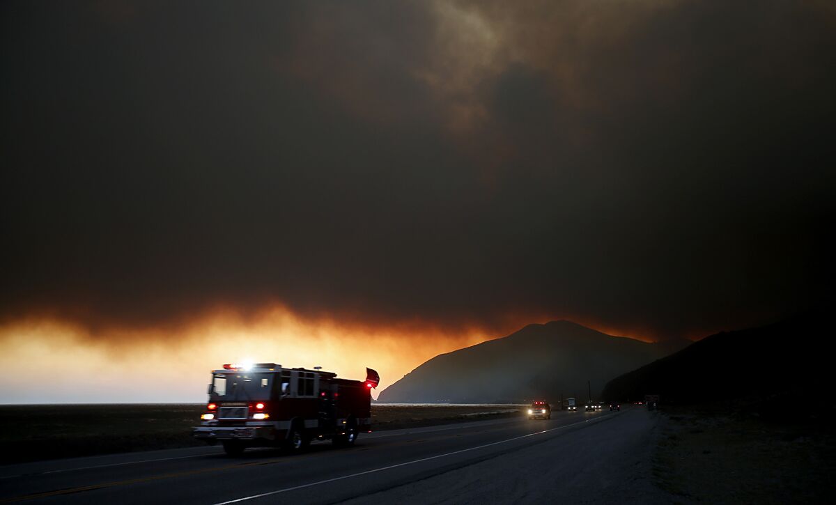 A fire engine races along Pacific Coast Highway near Point Dume as smoke blows out to the sea.