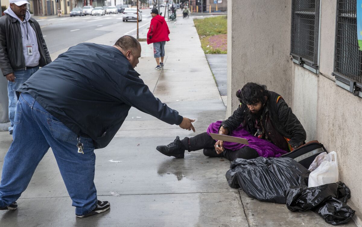 Outreach worker Ralph Gomez tosses a clipboard for a signature to homeless client Davis Soto during outreach in Los Angeles.