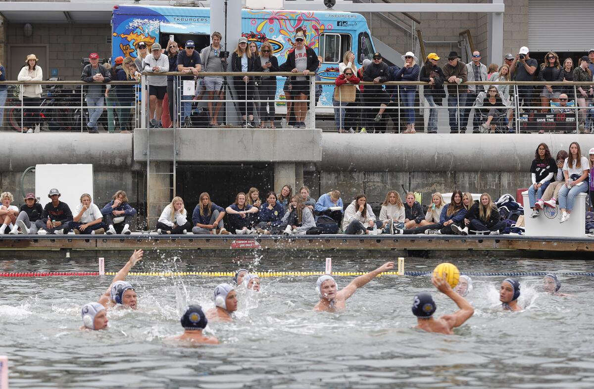 Members of the Newport Harbor and Corona del Mar boys' water polo teams battle in the bay in front of the crowd.