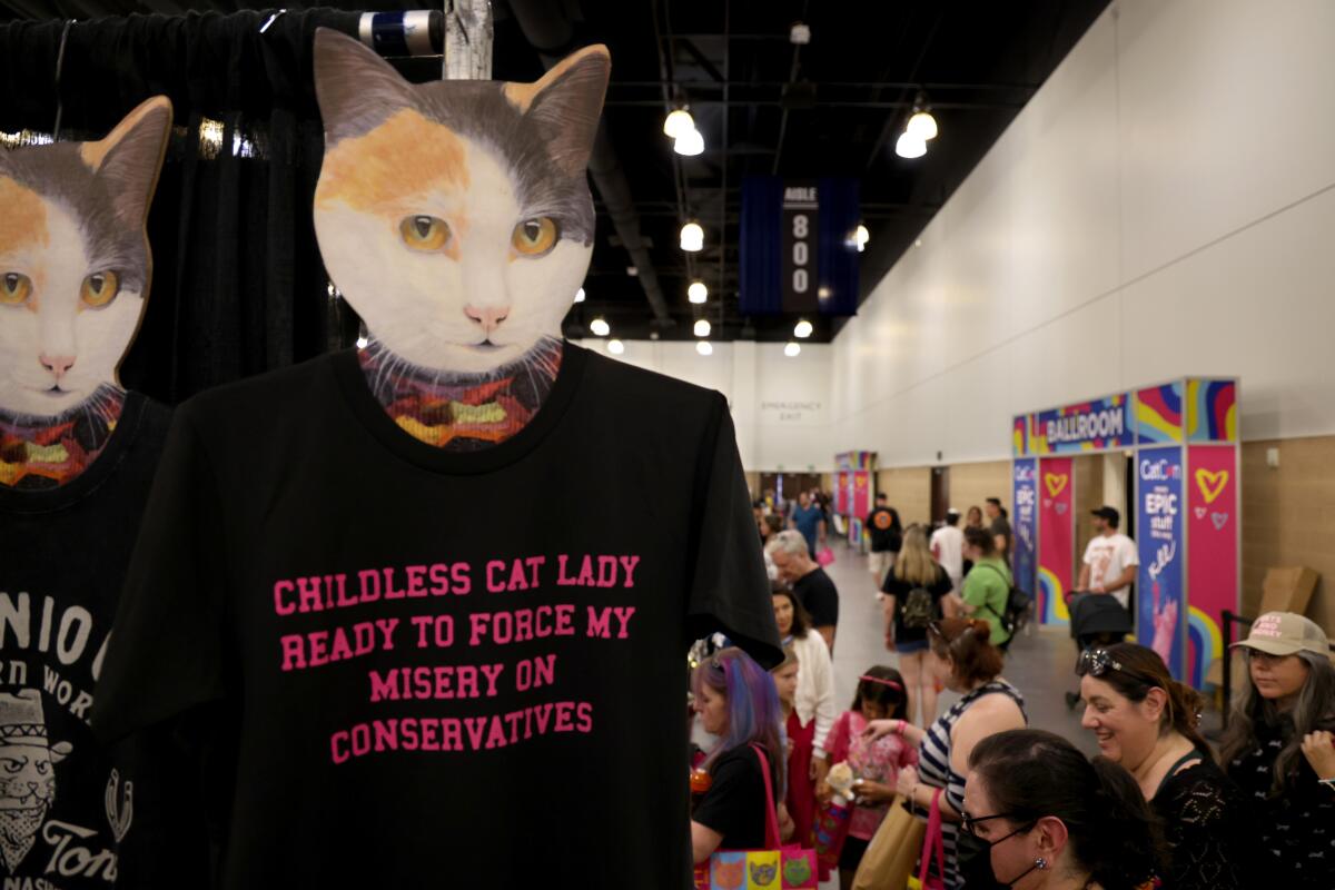 A T-shirt hanging below an image of a cat's head, with conference attendees in the background.