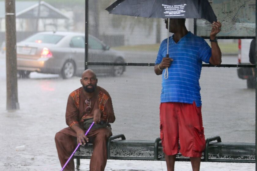 Residents sit under a bus shelter along a flooded Broad Street as heavy rain falls, Wednesday, July 10, 2019, in New Orleans. (David Grunfeld/The Advocate via AP)
