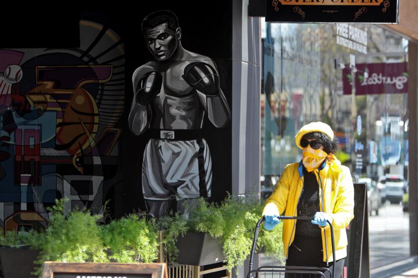 A woman wearing s face mask walks past an Over/Under Public House restaurant mural, as the world battles the novel coronavirus COVID-19, on the 300 block of San Fernando Rd. in Burbank on Saturday, April 11, 2020.