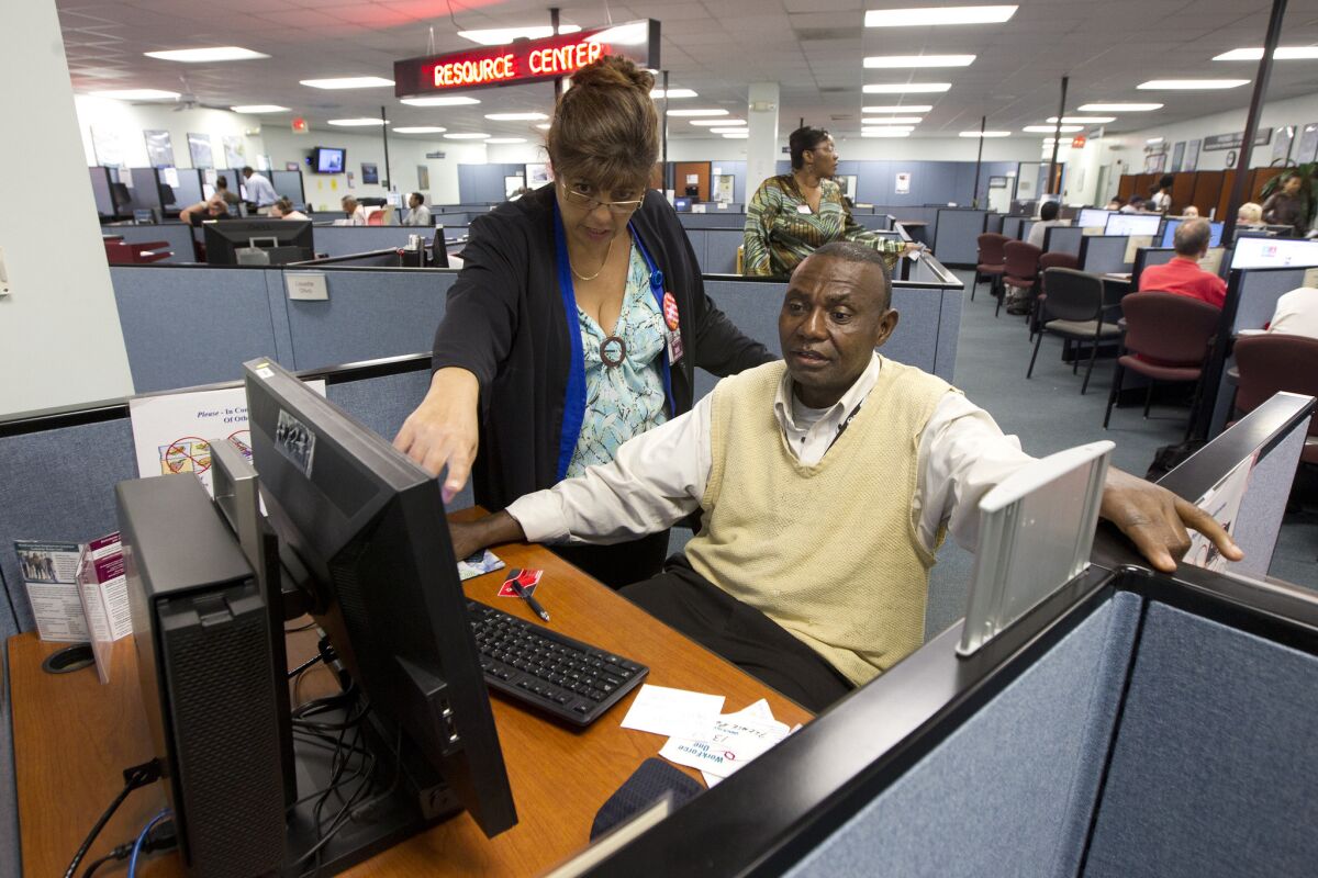 A WorkForce One staffer works with a client on job applications at an unemployment office in the Hollywood, Fla.