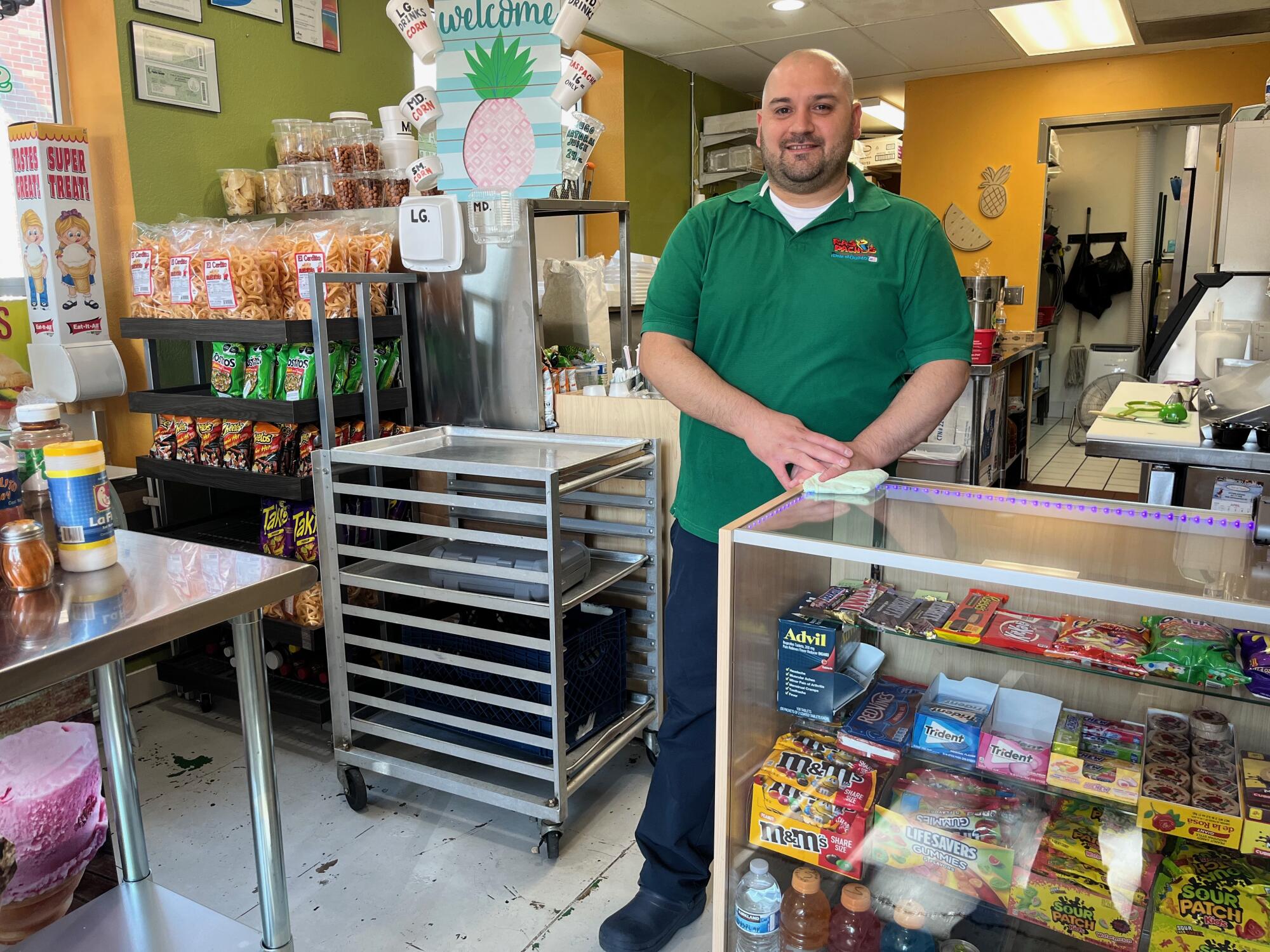 A man in a green shirt stands inside a shop with candy and snacks.