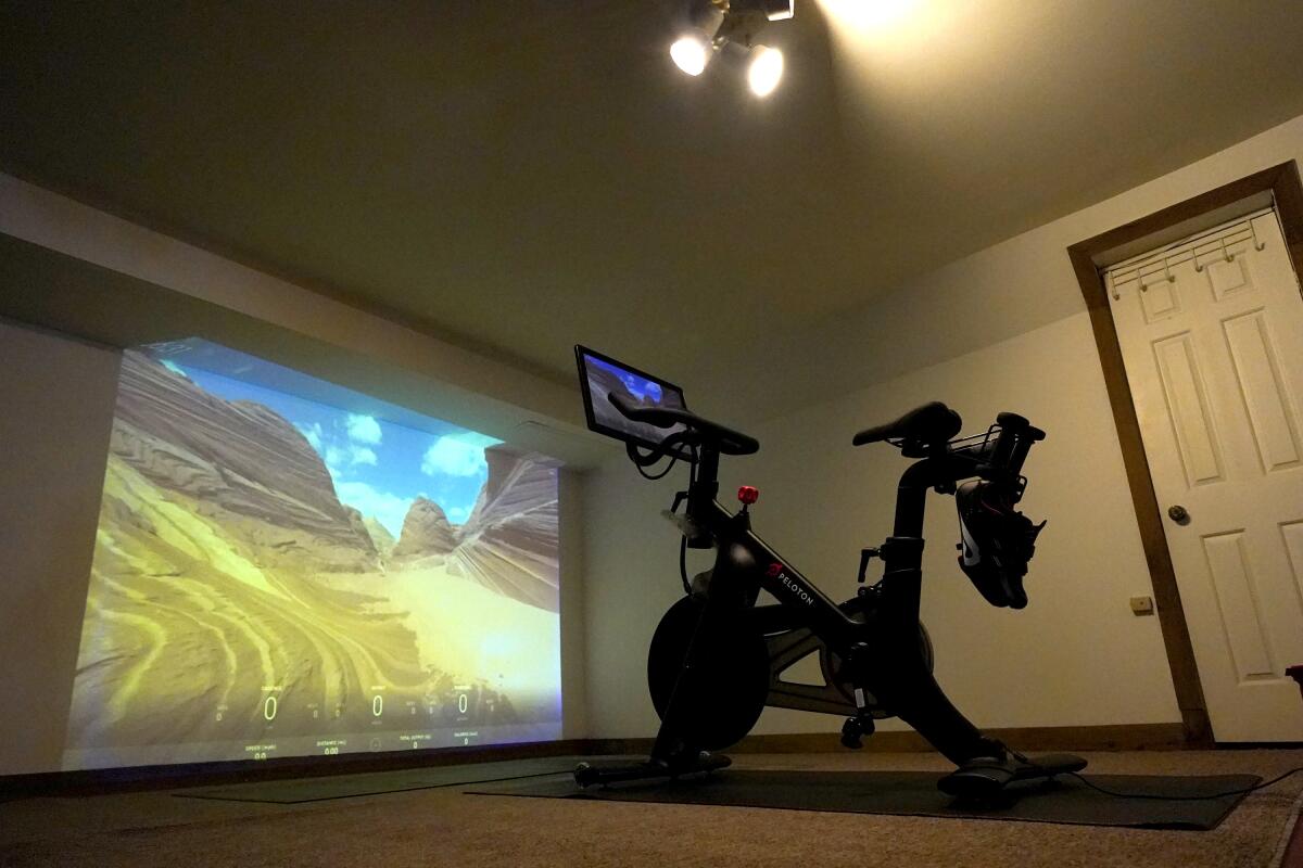 A projection of a desert scene is cast onto a wall near a Peloton fitness bike in a basement home gym.