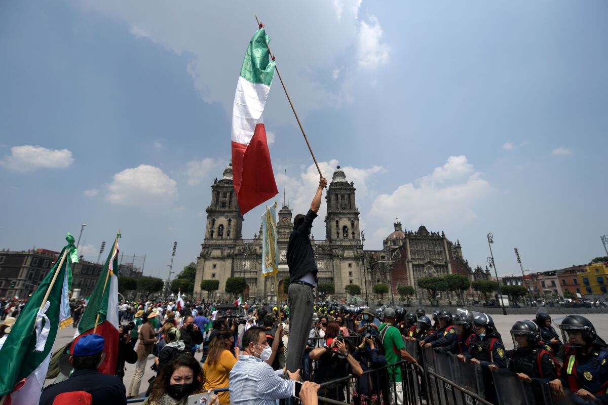 A member of the National Front Anti-AMLO (Frena) holds up a Mexican flag in front of a line of riot police 