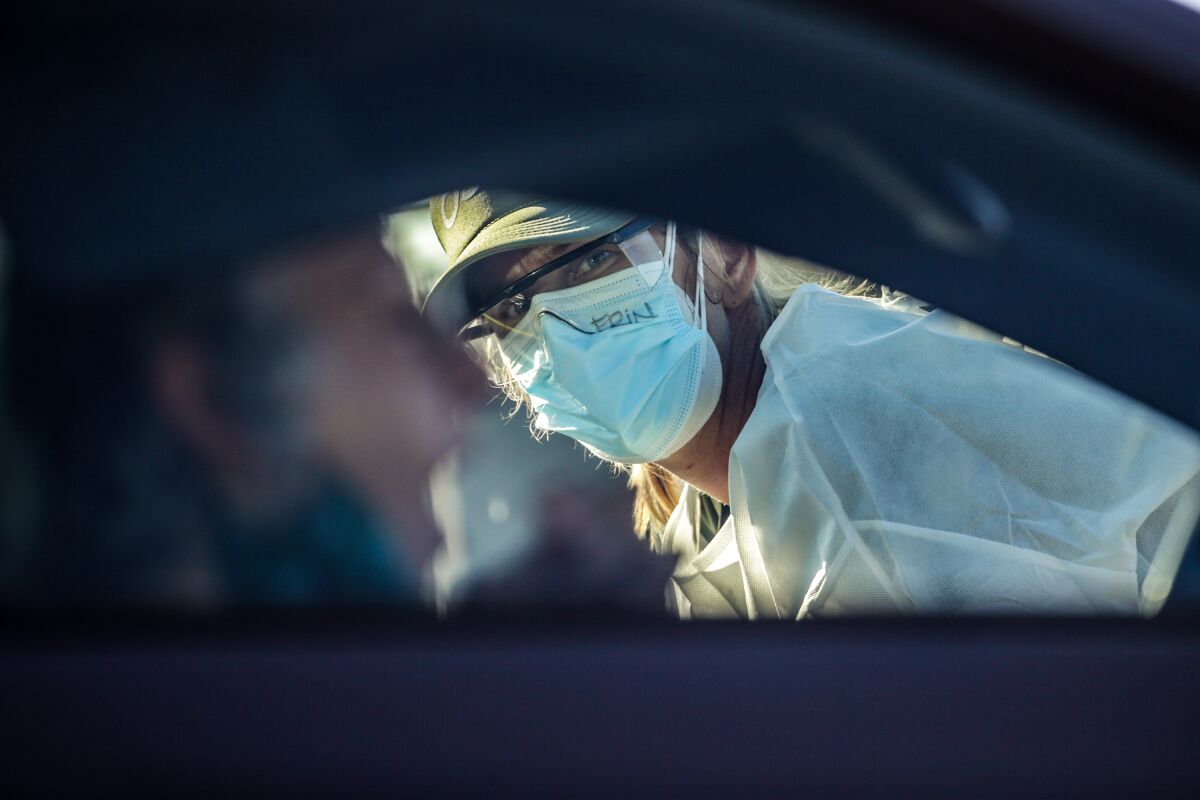A volunteer watches as a motorist performs a  coronavirus test at Dodger Stadium