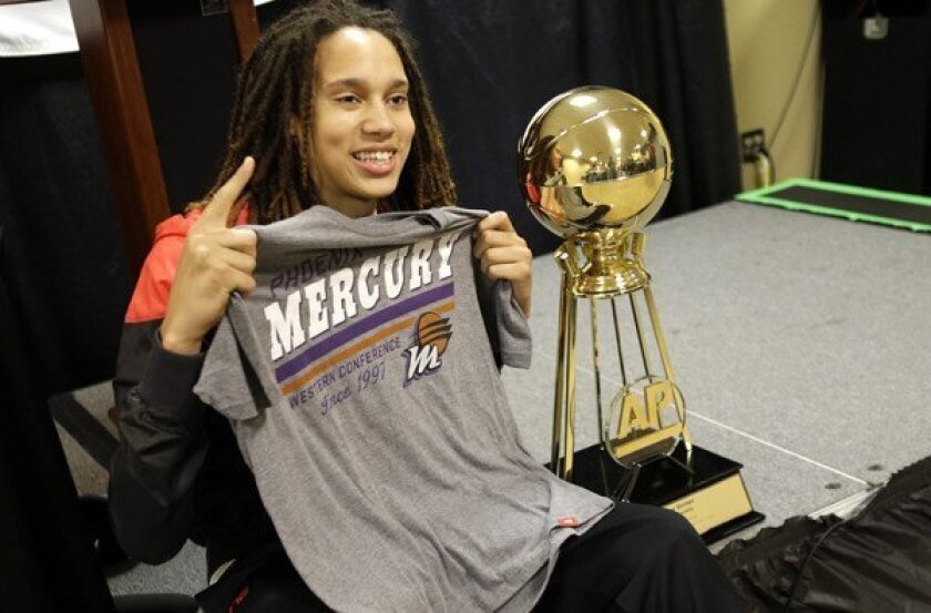 Brttney Griner holds up a Phoenix Mercury T-shirt as she poses next to the Associated Press Player of the Year Trophy during a news conference.