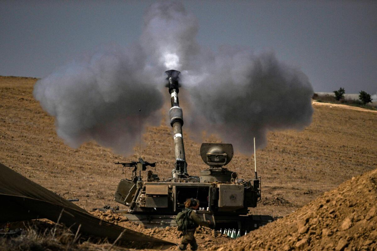 Smoke and a white light emerge from a howitzer as it fires into the distance