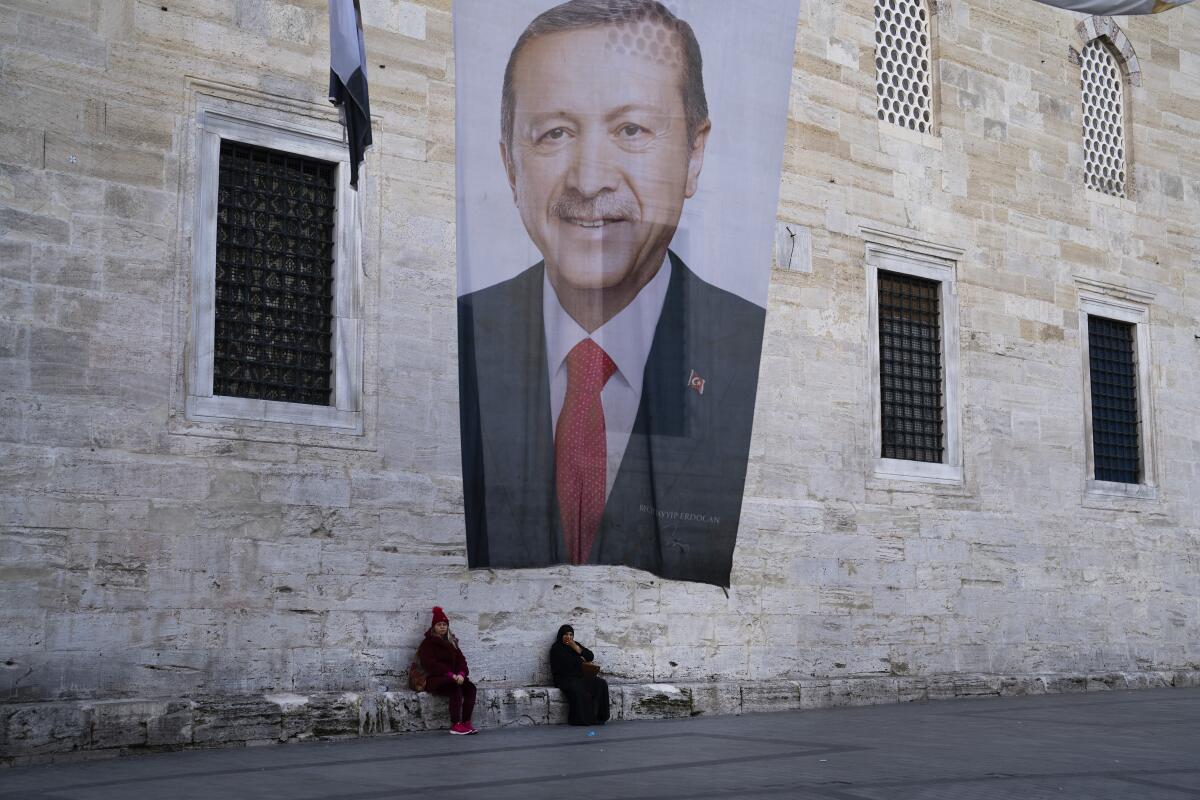 Two women sit near a campaign banner of Turkish President Recep Tayyip Erdogan in Istanbul.