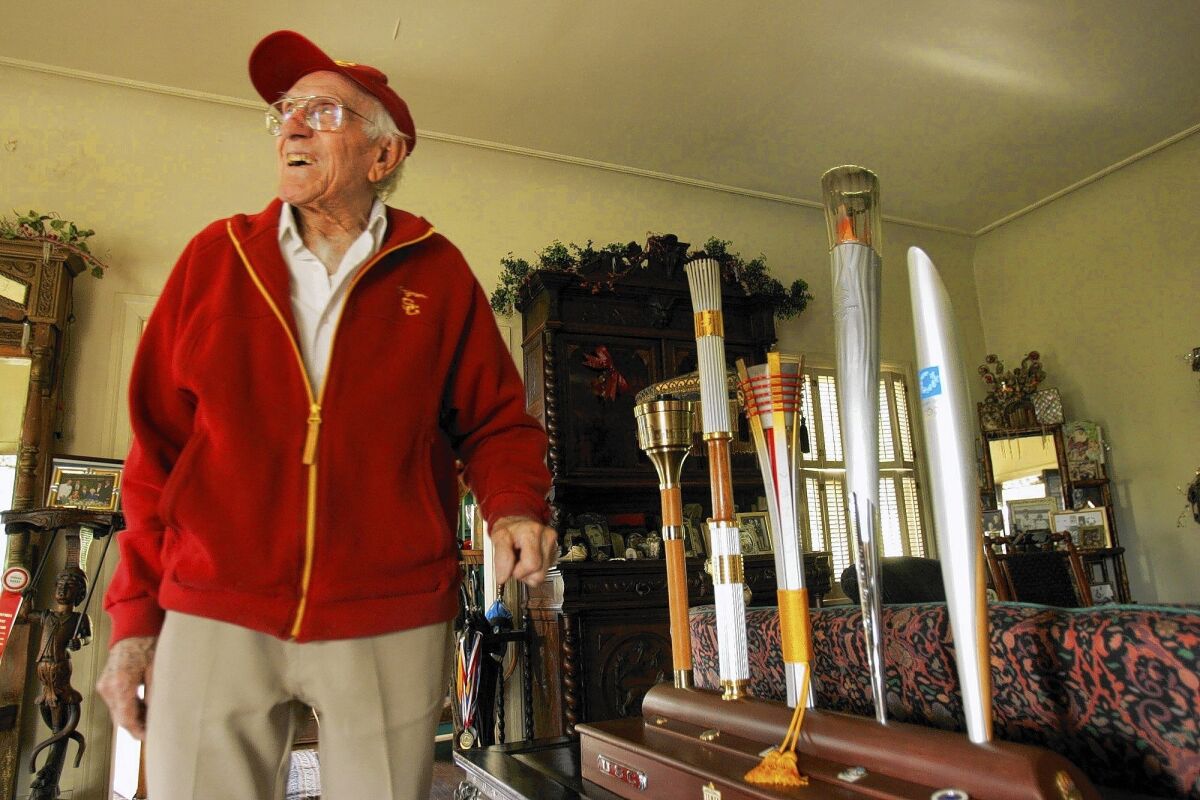 Louis Zamperini, shown next to some of the Olympic torches he helped carry in past Games, has been named grand marshal of the 2015 Tournament of Roses Parade in Pasadena.