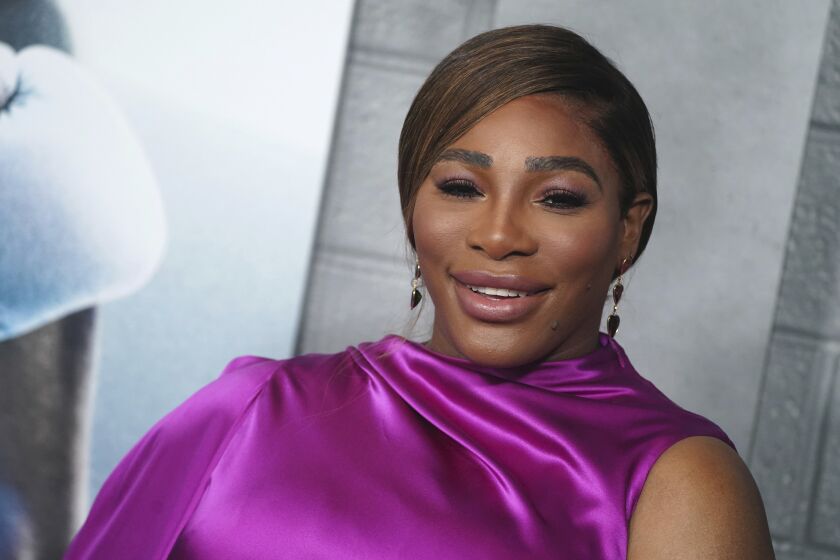 Serena Williams smiles while wearing a luxe purple garment
