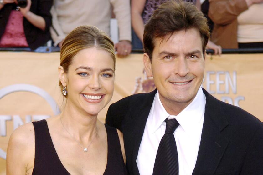 Denise Richards and Charlie Sheen smile while posing together in black formal attire.