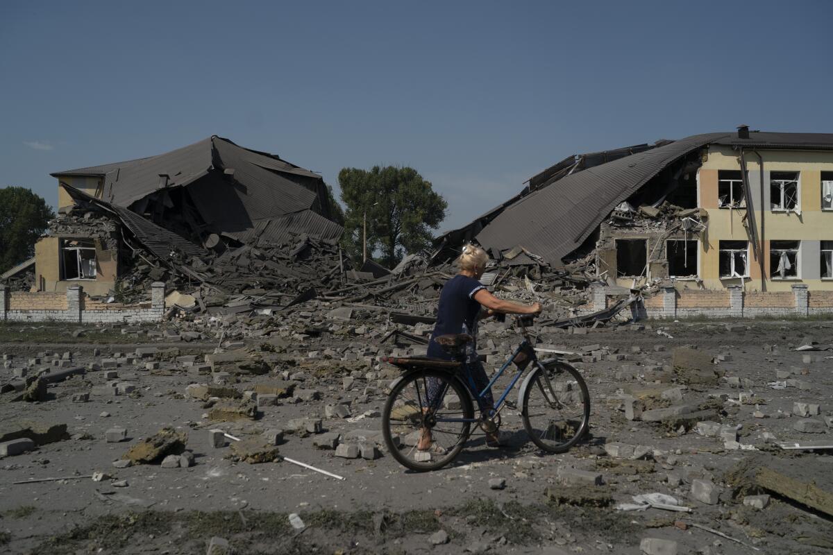 Una mujer camina con una bicicleta frente a una escuela que resultó dañada tras un ataque ruso 