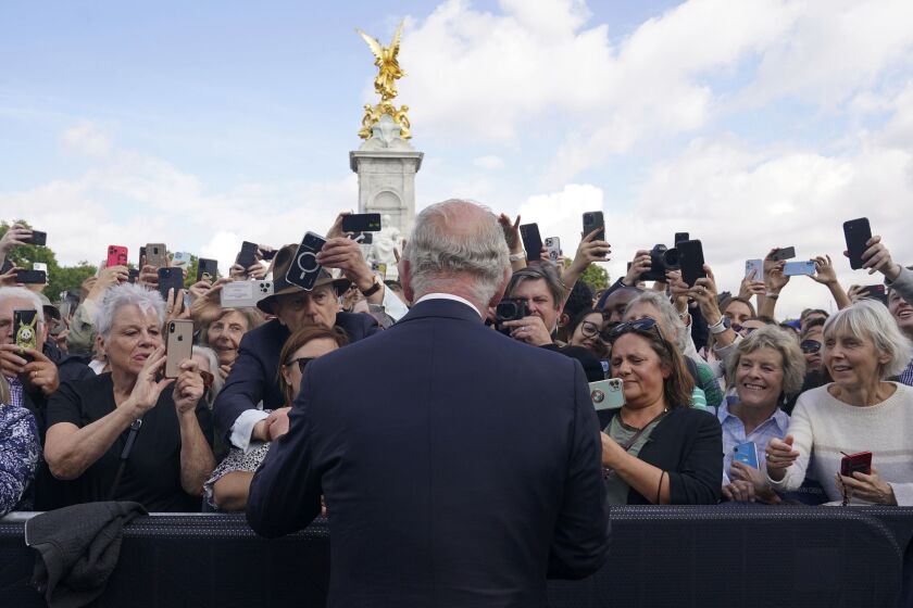 Britain's King Charles III, back to camera, greets well-wishers as he walks by the gates of Buckingham Palace following Thursday's death of Queen Elizabeth II, in London, Friday, Sept. 9, 2022. King Charles III, who spent much of his 73 years preparing for the role, planned to meet with the prime minister and address a nation grieving the only British monarch most of the world had known. He takes the throne in an era of uncertainty for both his country and the monarchy itself. (Yui Mok/Pool Photo via AP)