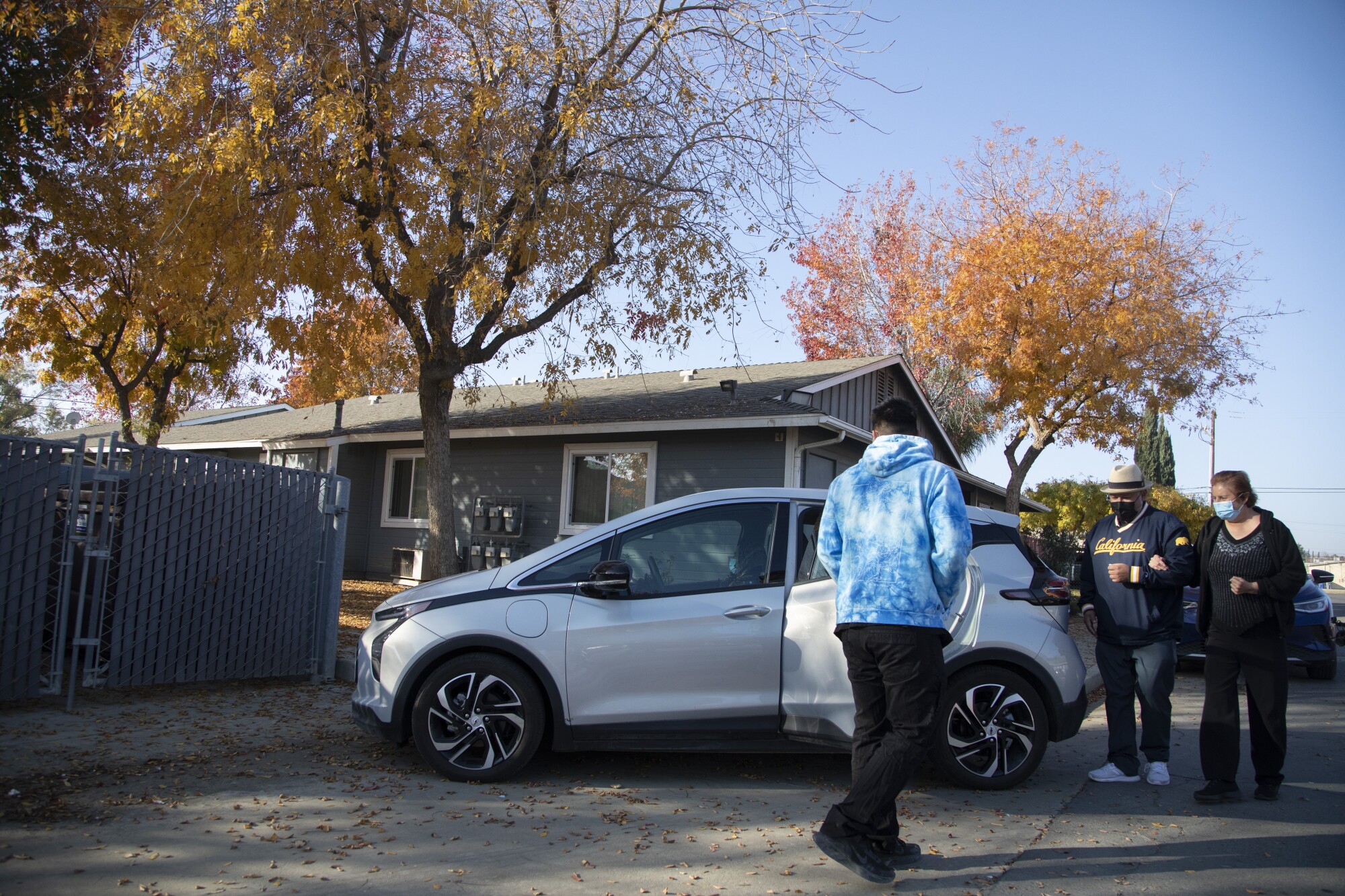 Driver Eddye Ramirez waits as Rey León helps Anna Maria Solorio to a Green Raiteros electric car. 