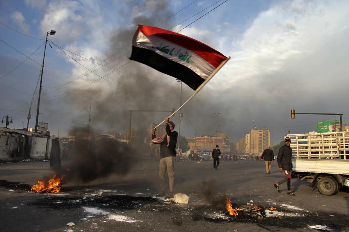 A protester waves the national flag as fires are set to close off streets near Baghdad's Tahrir Square