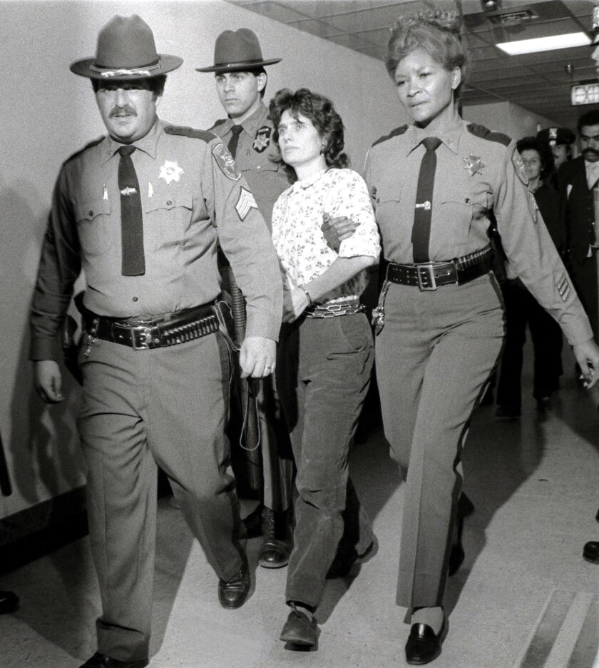 Three law enforcement officers walk with a woman.