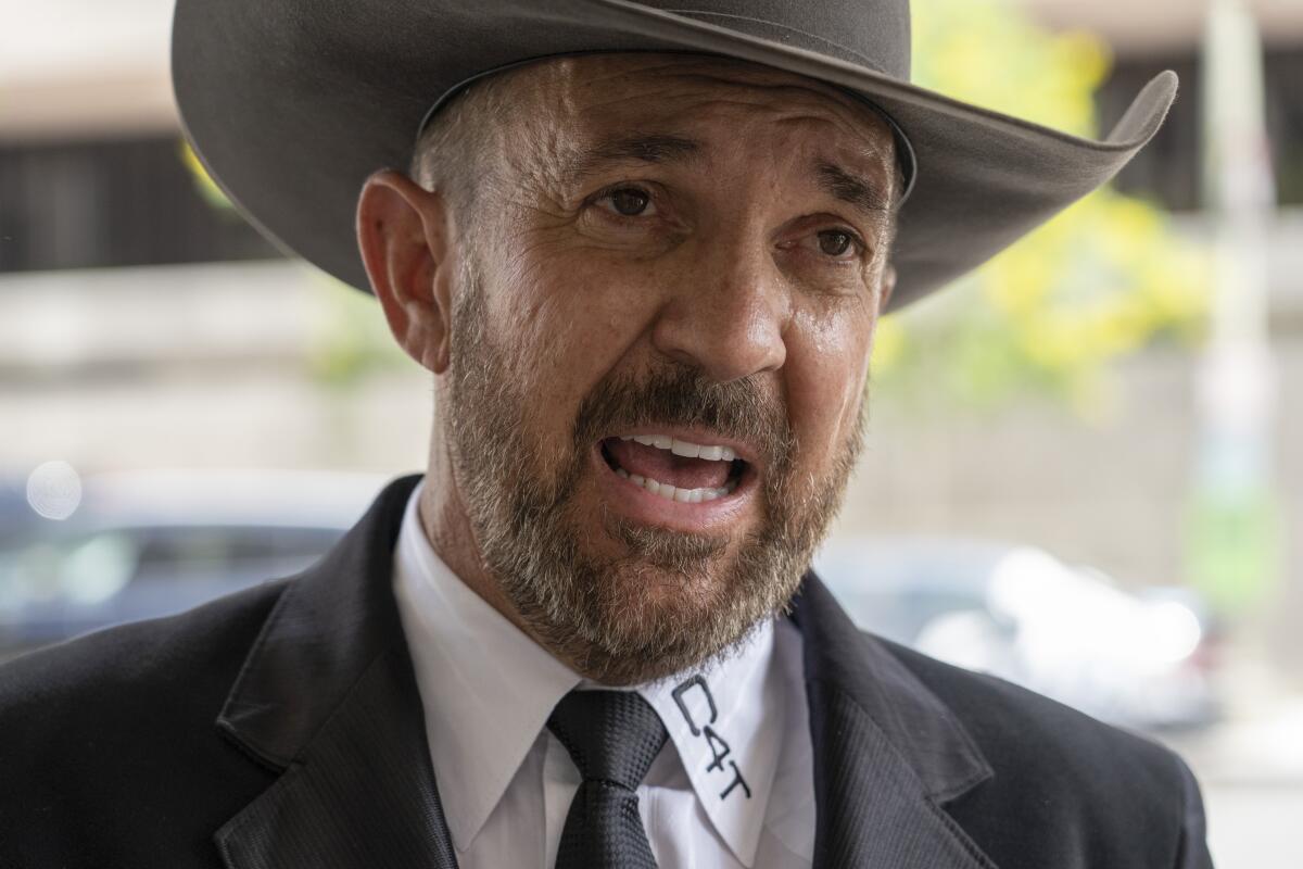 A man in a cowboy hat speaks to reporters