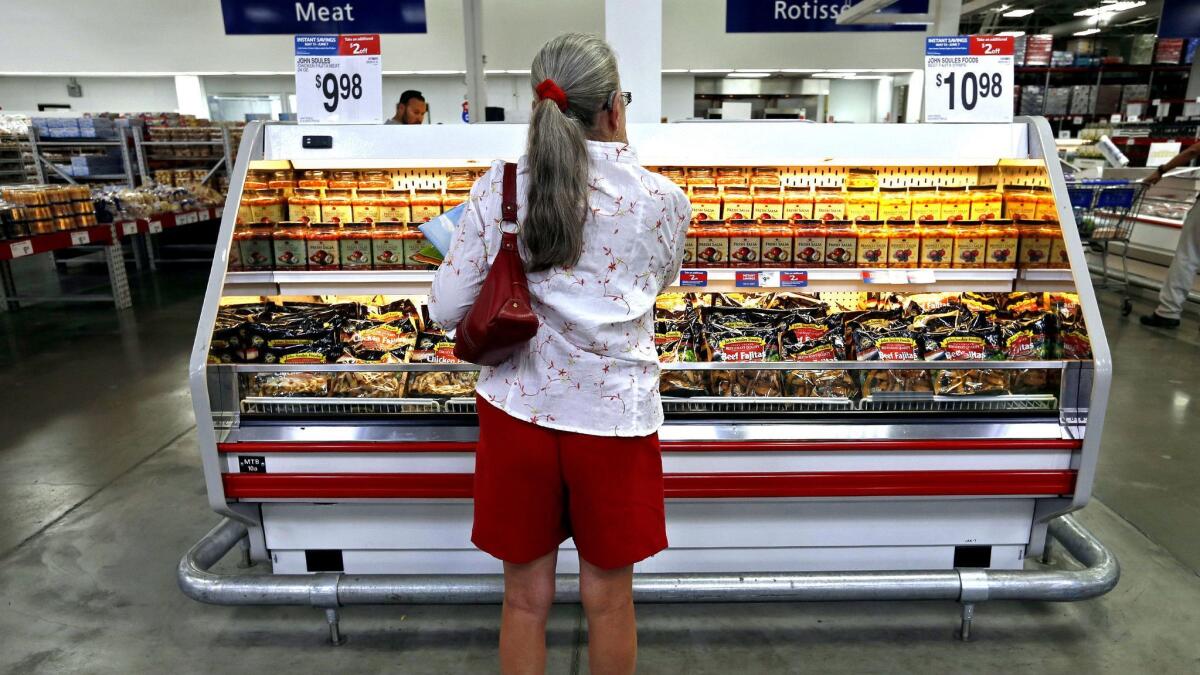 A woman looks at a refrigerated case in the meat section of a grocery store.