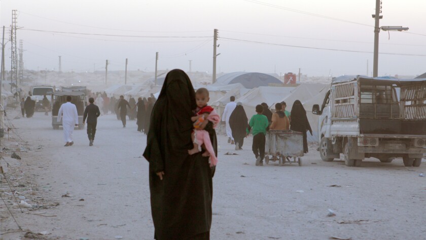 A woman in a black burqa carries a child on a dusty road in the documentary “Sabaya.”