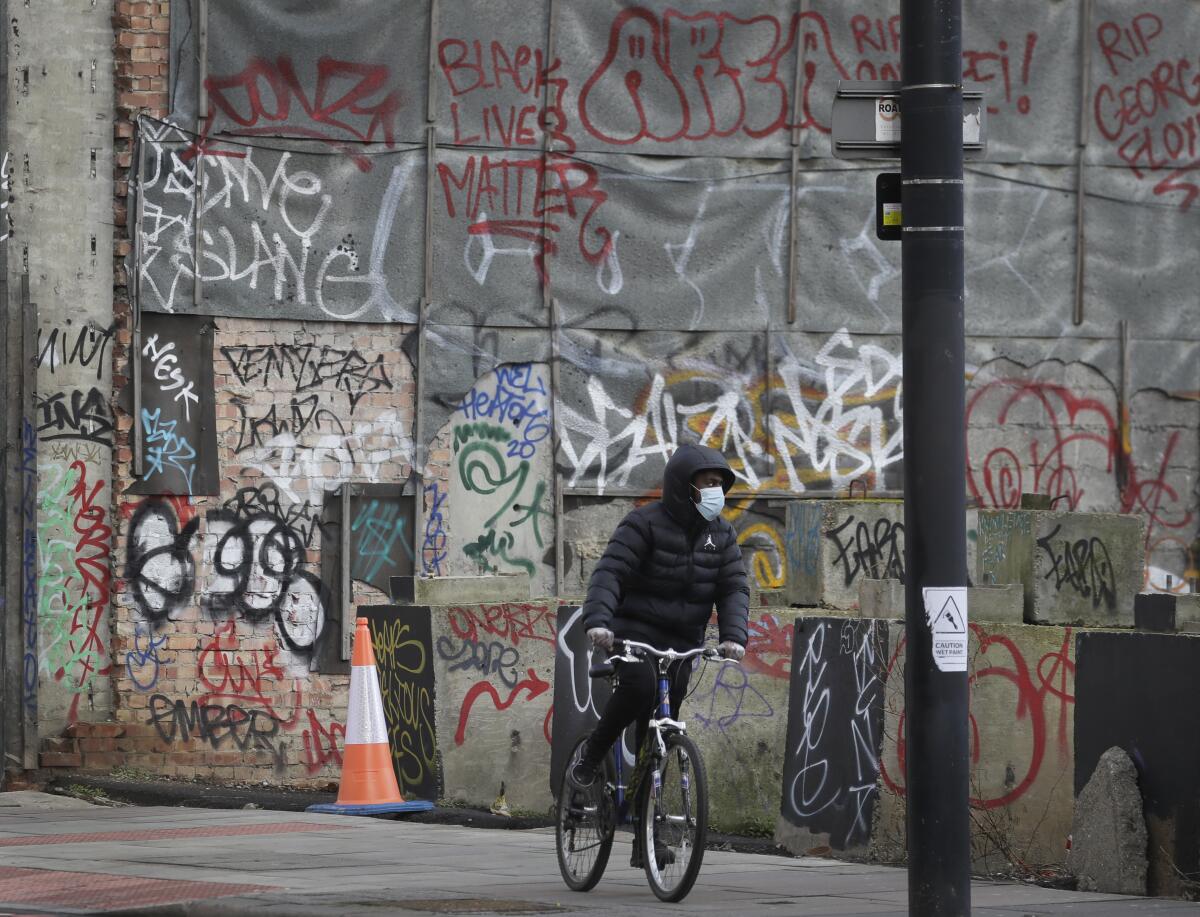 Un ciclista usa una mascarilla mientras pasa por un muro con pintas en Londres,