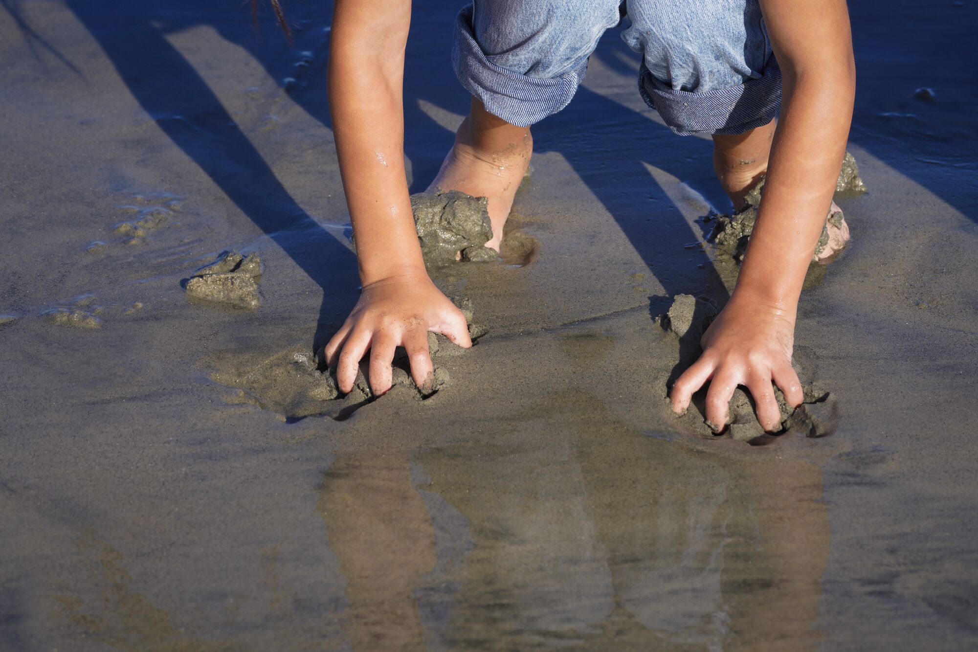 a young girl digs her hands into the sand at the beach