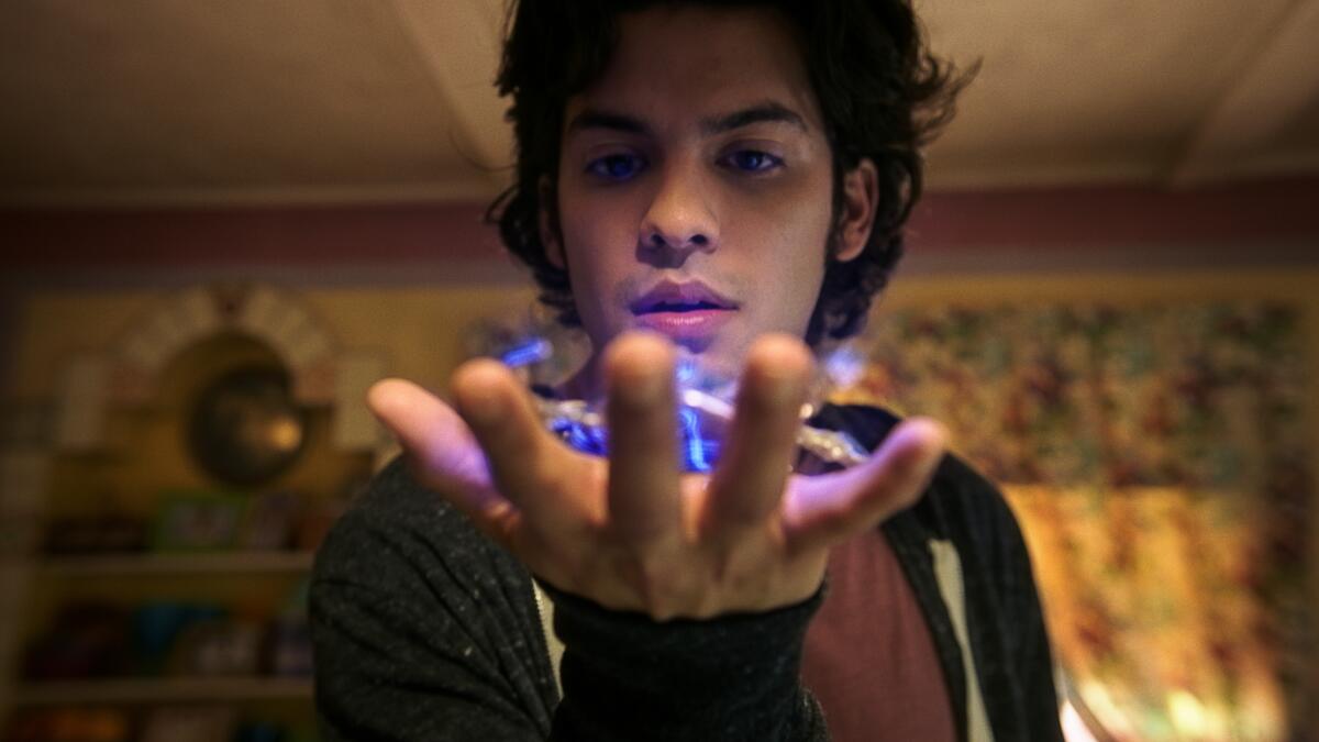 Xolo Maridueña holds a glowing purple object in his hand and stares at it.