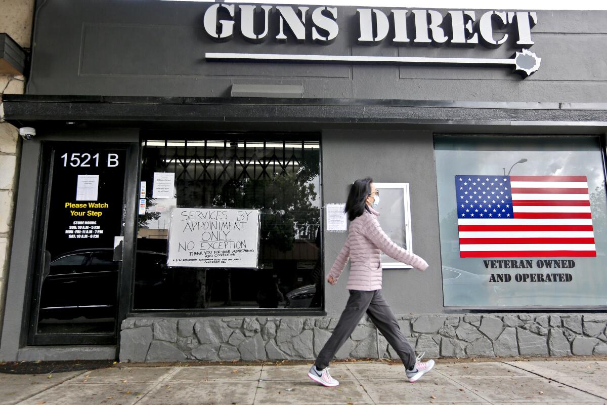 A woman walks in front of a store called Guns Direct, with a sign in the window saying "services by appointment only"