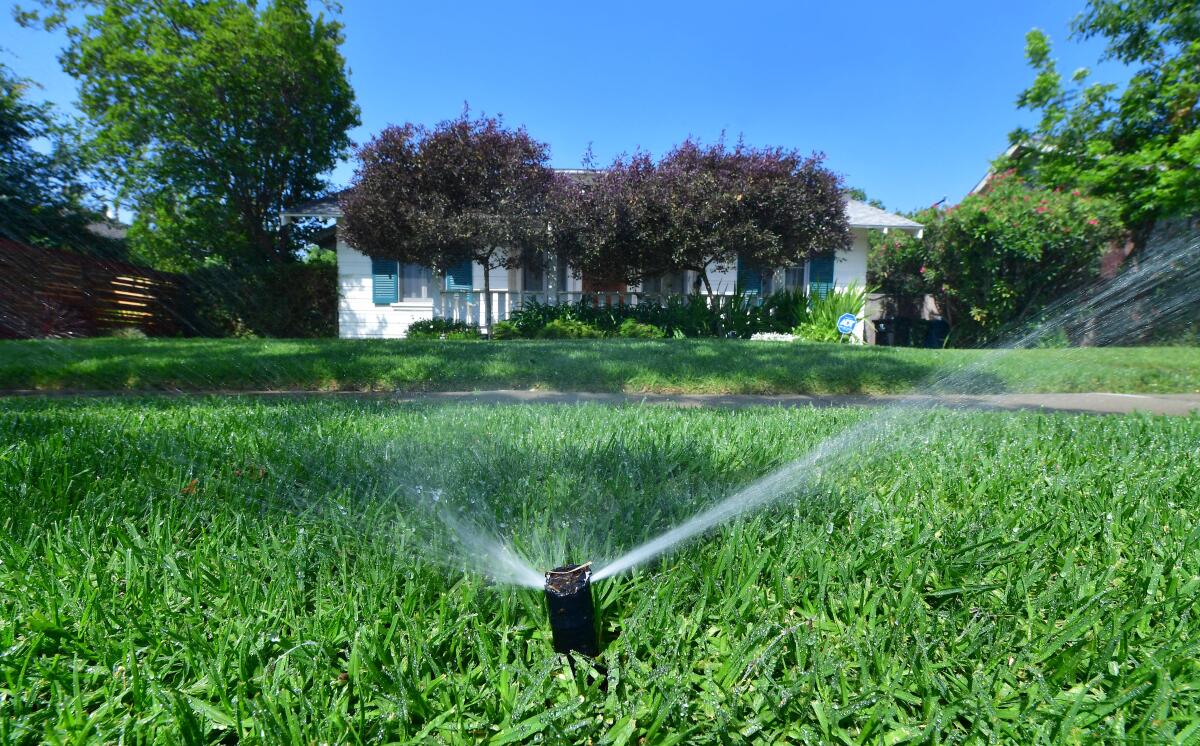 An automated sprinkler waters grass in front of homes in Alhambra.