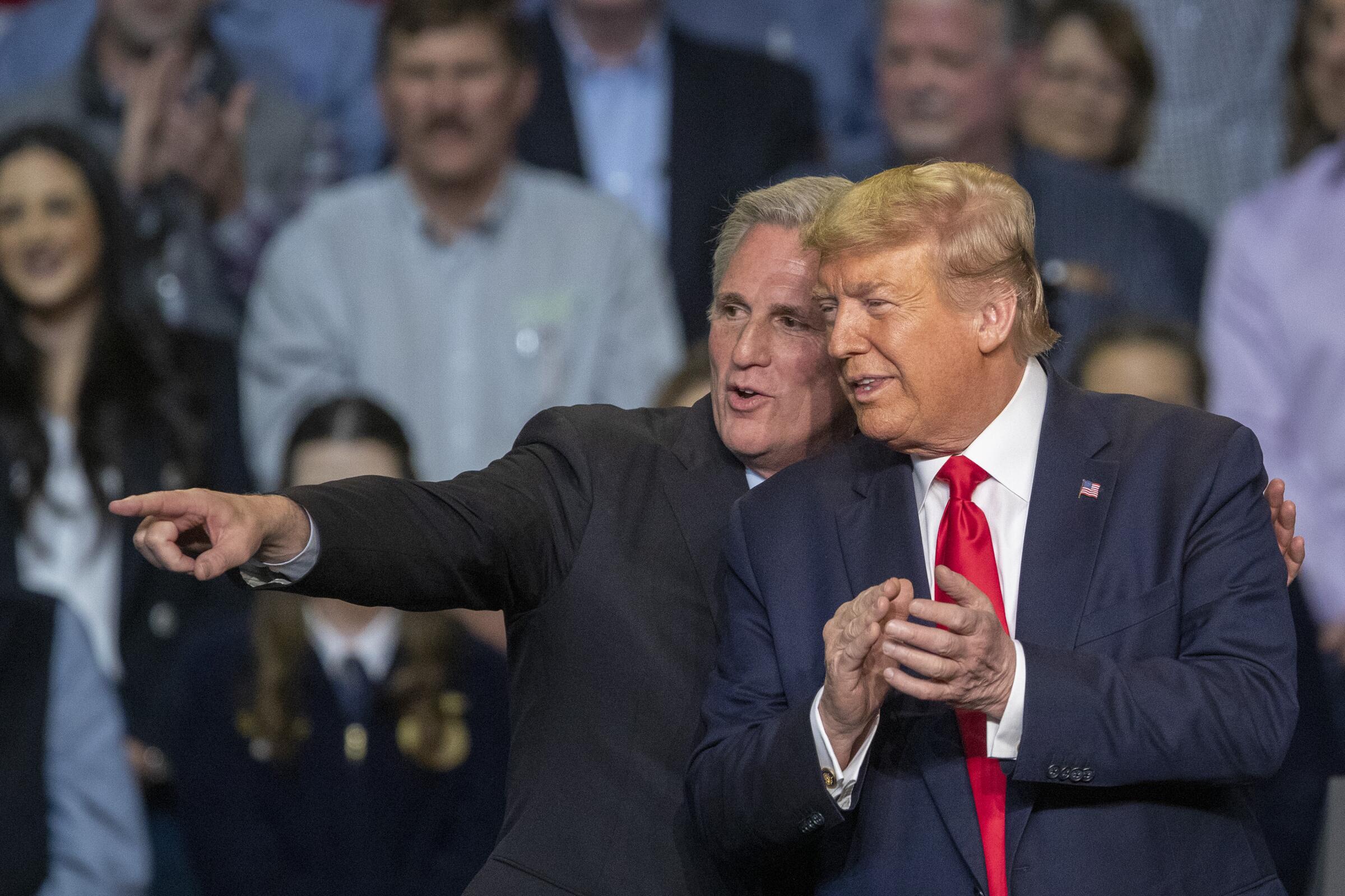 Kevin McCarthy stands with an arm around Donald Trump in front of an audience, pointing away as Trump looks and claps