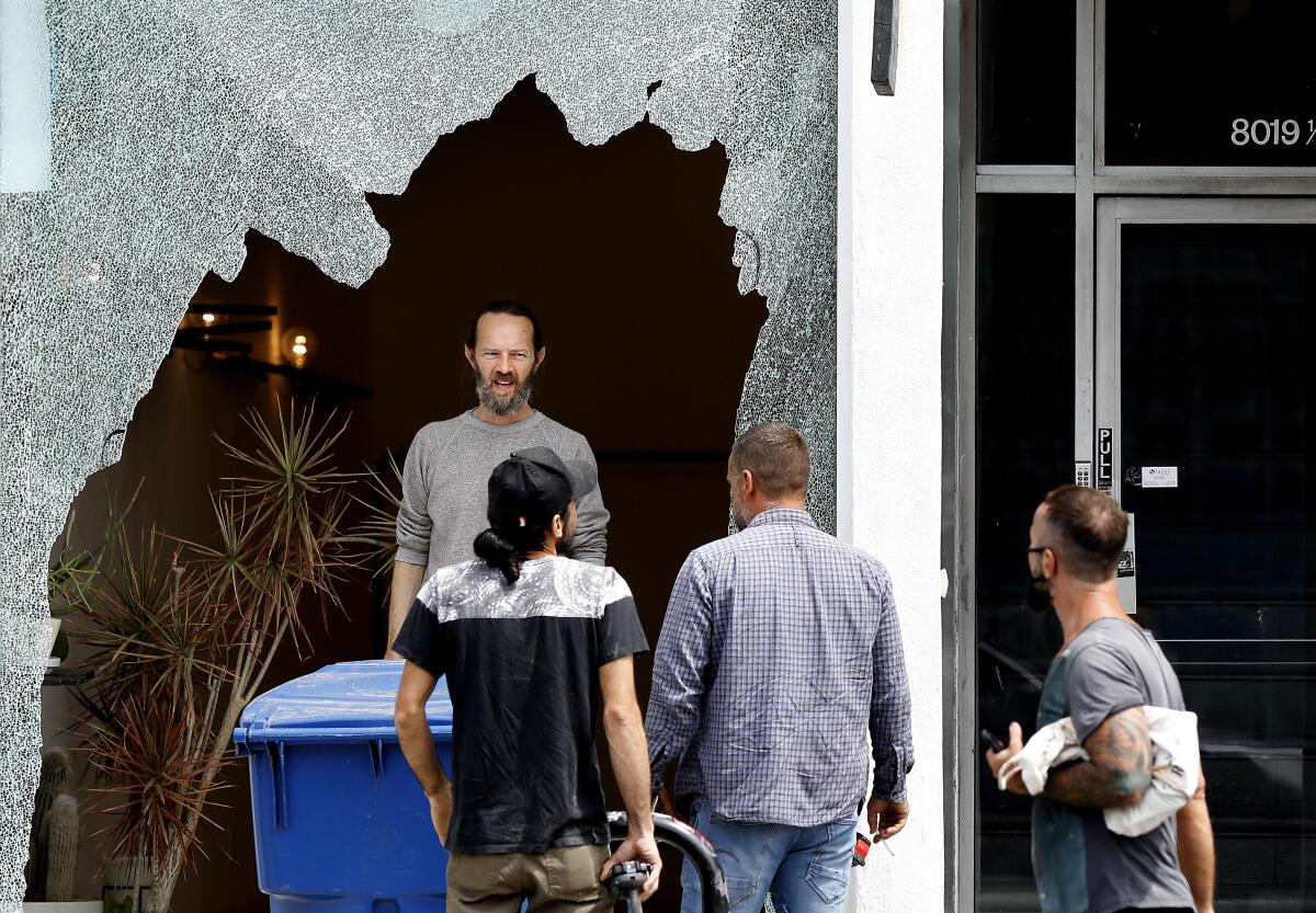People gather in front of a shattered storefront window