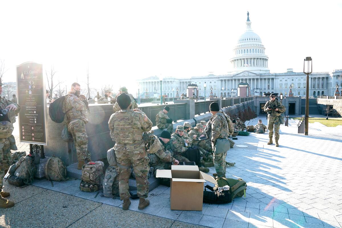 A group of National Guard troops in camo fatigues rest on a wall outside the U.S. Capitol